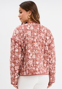 Giacca trapuntata in morbido tessuto rosa con motivo floreale, maniche corte e bordo a costine, con una vestibilità rilassata e superficie strutturata.