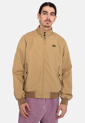 Tan jacket with a high collar, zippered front, and side pockets. Features ribbed cuffs and a small multi-colored logo on the chest.