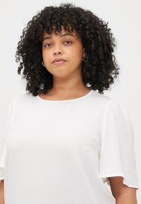 White blouse with short, puffed sleeves, made of textured fabric. Rounded neckline and relaxed fit, suitable for casual wear.