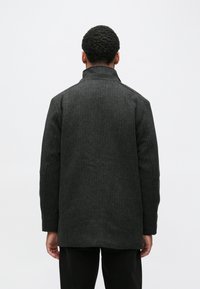 Casaco cinza de mistura de lã com gola alta e ombros estruturados. Apresenta corte reto, costuras visíveis e design de comprimento médio.