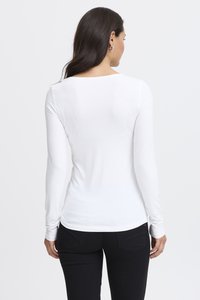 Pitkähihaisen valkoisen paidan, joka on tehty sileästä kankaasta, jossa on pyöreä kaula-aukko ja istuva leikkaus, parina mustat housut.