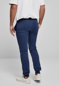 Marineblå træningsbukser med slim fit, lavet af blødt bomuldsstof, med sidelommer og ribbet manchet, kombineret med hvide sneakers.