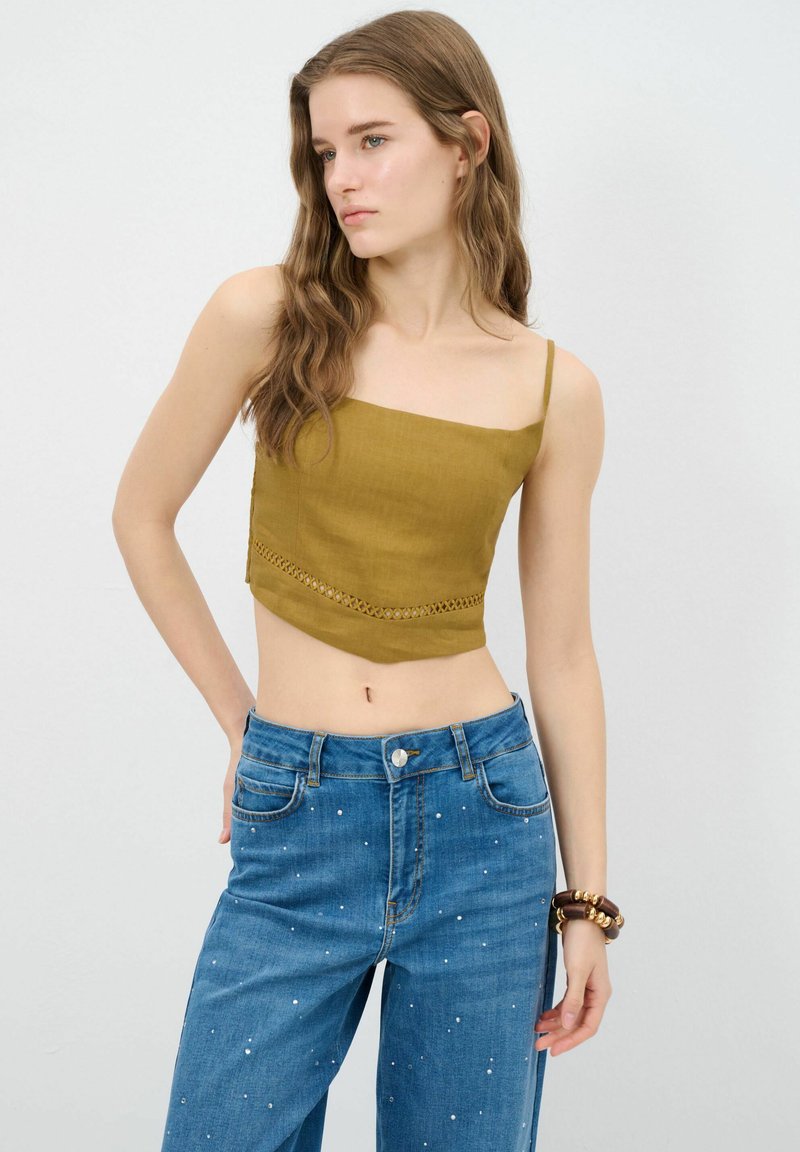 Khaki cropped top met dunne bandjes en kantafwerking, gecombineerd met mid-rise blauwe jeans versierd met witte stippen.