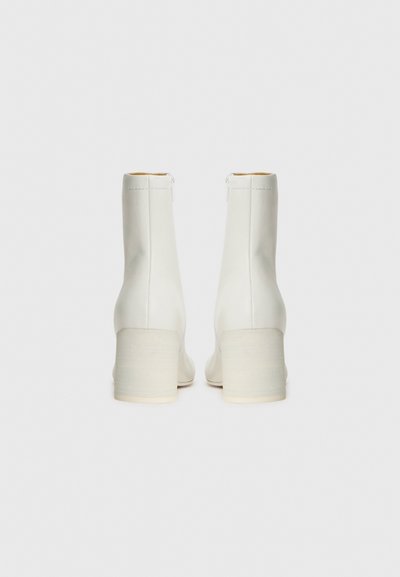 Bottines blanches en cuir lisse, avec une tête arrondie et un talon carré. Présentent une fermeture éclair sur le côté et un design minimaliste.