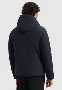 Marineblauwe pufferjack met een capuchon, met een gladde afwerking en een subtiele logo op de achterkant. Het ontwerp is korter en heeft elastische manchetten.