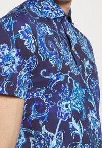Pánská polo tričko s krátkým rukávem v tmavě námořnické barvě, se živým modrým květinovým a spirálovým vzorem, s límcem a knoflíkovou légou.