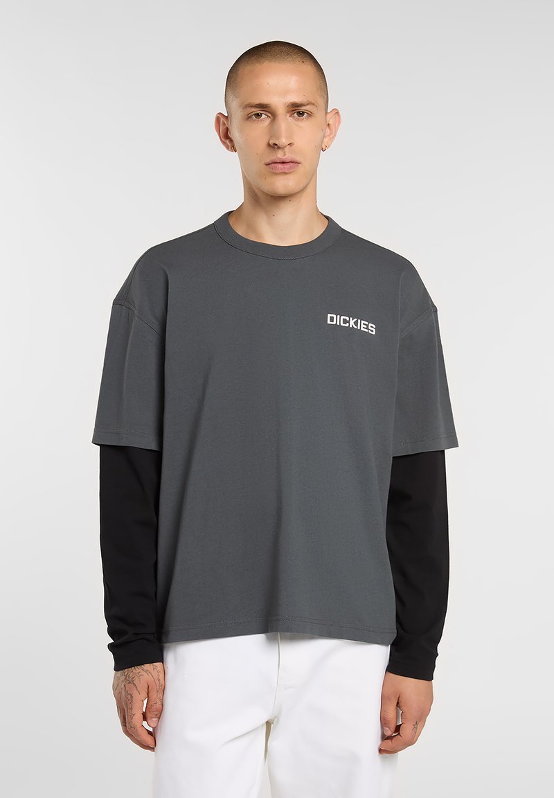Short-sleeve grey t-shirt with a crew neck, featuring white "DICKIES" logo. Black long sleeves underneath, visible at cuffs. Smooth, cotton material.