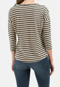 Woman wearing beige and black horizontal striped long-sleeve shirt and blue jeans, shown from the back.