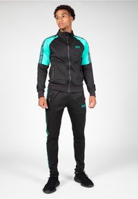 Tuta nera con accenti turchesi, giacca con zip, vita elastica e pantaloni aderenti, con dettagli del logo e tasche laterali.