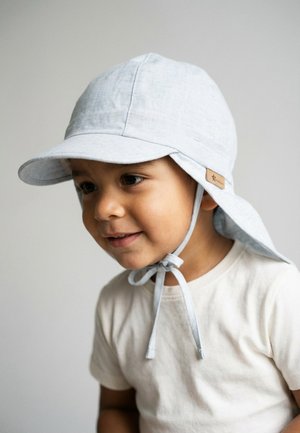 Young child wearing a light blue sun hat with neck flap and chin ties, smiling slightly, dressed in a plain white T-shirt.