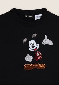 T-shirt noir avec un design de Mickey Mouse ornée de sequins en rouge, blanc et noir, avec des accents orange sur les chaussures. Encolure ronde.