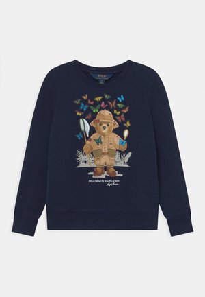 Marineblauer Pullover mit einer Grafik eines Bären in Safari-Kleidung, umgeben von bunten Schmetterlingen. Hergestellt aus weichem Stoff mit Rundhalsausschnitt.