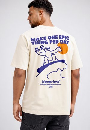 Man wearing cream t-shirt with graphic of cartoon surfer, sun, and text "MAKE ONE EPIC THING PER DAY" and "Neverless" on back.