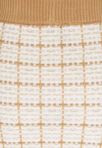 Tissu beige côtelé au-dessus d’un textile tissé blanc et beige avec un motif en quadrillage et quelques fils métalliques.