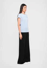 Lichtblauw T-shirt met korte mouwen en scripttekst, gecombineerd met zwarte wijde trousers en witte sneakers. Gladde stof met een aangesloten ontwerp.