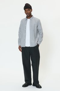 Srajca z gumbi s črtami v beli in mornarsko modri barvi, kombinirana z enobarvno belo majico, črnimi širokimi hlačami in črnimi čipkami za vezanje.