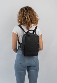 Fekete hátizsák, tartós anyagból készült, két felső fogantyúval, állítható pántokkal és minimalista designnal, elülső logóval.