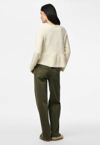 Pull en laine beige avec un bas peplum, associé à un pantalon droit vert olive. Le pull possède un col rond et des manches longues.