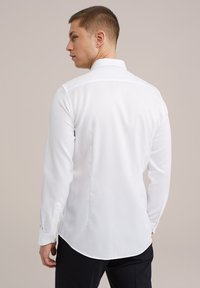 Camisa blanca de manga larga con cuello extendido, dobladillo recto y puños con botones. Tejido suave con un diseño limpio y clásico.