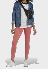 Rosa leggins, vita sneakers, en grå t-shirt och en blå denimjacka. Outfitten inkluderar en svart axelväska med en dragkedjefunktion.