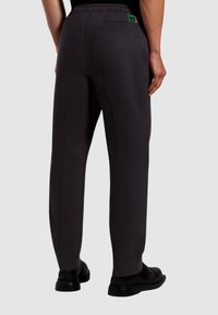 Pantaloni grigi scuri realizzati in un tessuto morbido con una vita elastica, dotati di una toppa con logo verde sul retro e un design a gamba dritta.