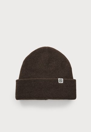 Bruine geribbelde gebreide muts met een omgeslagen rand en een klein wit logo-label aan de zijkant. Gemaakt van zacht, warm materiaal.