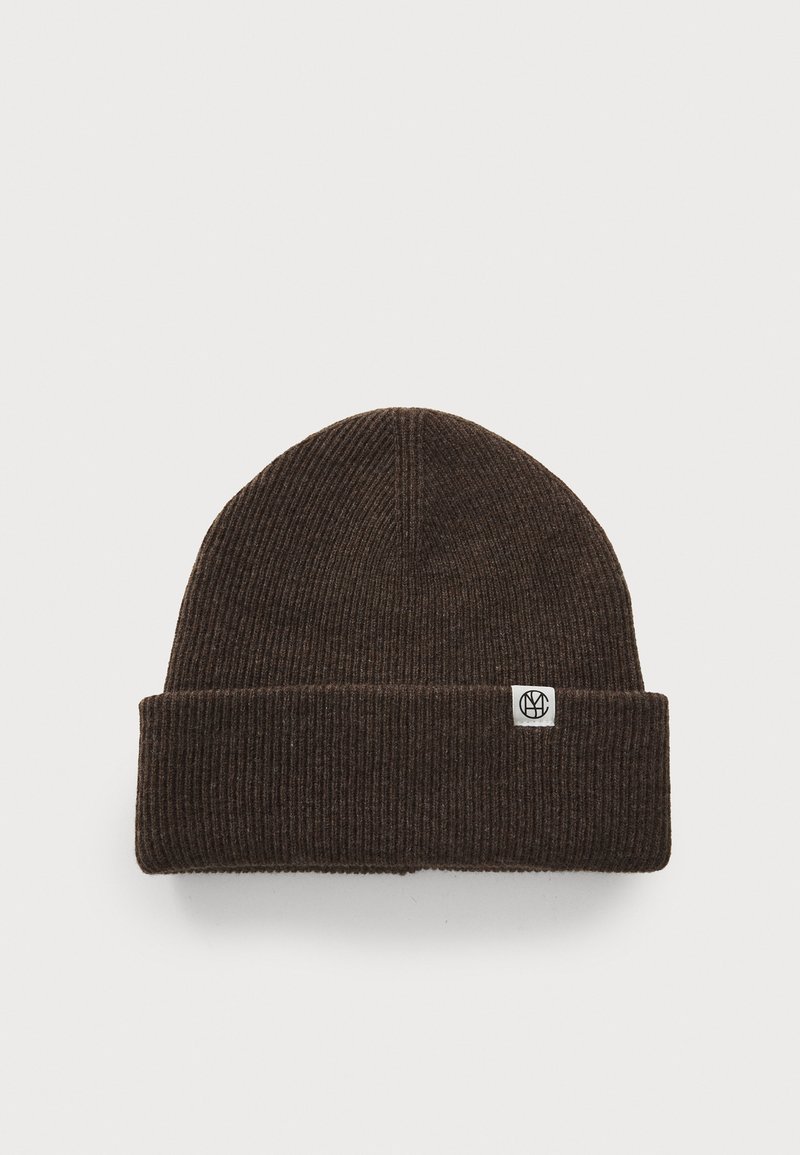 Brown ribbed knit beanie with a folded cuff and a small white logo tag on the side. Made of soft, warm material.