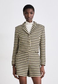 En svart och gul rutiga kavaj och shorts-set med en strukturerad design. Har en kortad silhuett och knapppdetaljer. Texturerad tyg.
