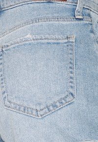 Ljusblå denimjeans med en urtvättad finish, som har en bakficka och subtila sömnadsdetaljer, med ett slitet område nära överkanten.