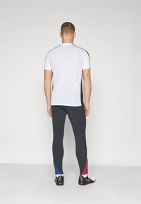 Completo sportivo composto da una maglietta bianca a maniche corte con accenti neri e pantaloni neri a coste con pannelli laterali blu e rossi.