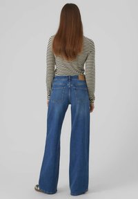 Jeans de mezclilla azul de pierna ancha con un lavado claro, que cuentan con un parche de cuero marrón en la parte trasera y un diseño de cinco bolsillos. Top de manga larga a rayas.