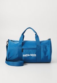 Blaue Reisetasche aus glattem Stoff, mit einem Reißverschlussfach, doppelten Tragegriffen und einem abnehmbaren Gurt. Logo in Weiß gedruckt.