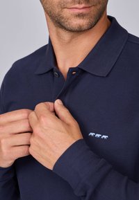 Polo bleu marine en coton texturé. Pourvu d'un col et de trois petits motifs d'animaux brodés sur la poitrine gauche.