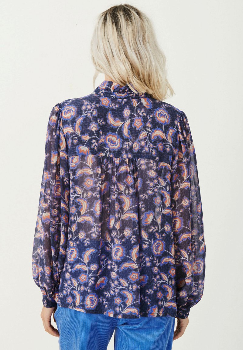 Bluzka w kwiatowy wzór z przezroczystej tkaniny, w odcieniach niebieskiego i pomarańczowego. Długie, bufiaste rękawy oraz marszczony detal na plecach.