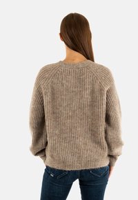 Maglione lavorato a maglia grossa in beige chiaro con texture a coste, spalle scese e scollatura rotonda. Indossato con jeans slim blu scuro.