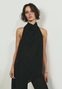 Top halter negru cu un decolteu drapat, având o țesătură texturată cu mici sclipiri metalice subtile și o tăietură asimetrică la margine.