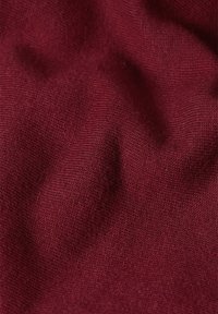 Bordeaux gebreide stof met een gladde textuur, voorzien van een fijne weefstructuur en lichte rek, die zachte, gedrapeerde plooien creëert.