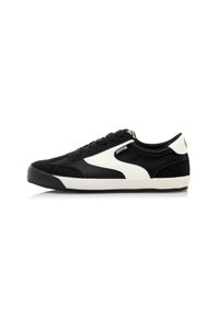 Zapatilla en blanco y negro con un upper de ante y cuero, diseño de cordones, panel texturizado y suela de goma. Presenta una marca en el lateral.
