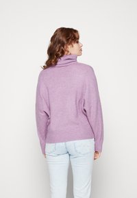 Un pull col roulé violet surdimensionné avec une finition douce et texturée. Associé à des jeans ajustés bleu clair. Le design présente des épaules tombantes.
