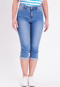 Pantalones capri de mezclilla azul claro con dobladillos enrollados, diseño de cinco bolsillos, desvanecimiento sutil y cintura alta, combinados con zapatillas blancas.