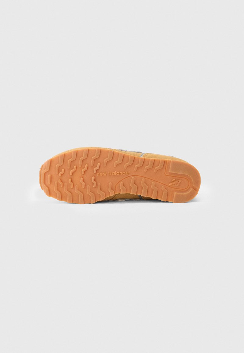 Semelle en caoutchouc orange avec un motif de semelle texturé, présentant le logo "new balance". Partie supérieure en suède visible sur les bords, avec des accents gris.