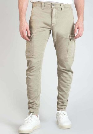Pantalones cargo beiges con un corte ajustado, que cuentan con bolsillos laterales, una cintura estándar y un material suave de mezcla de algodón. Combinados con zapatillas blancas.