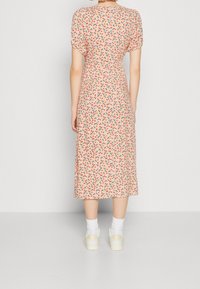 Mujer de pie, vistiendo un vestido midi con mangas cortas abullonadas y un estampado floral pequeño multicolor, combinado con calcetines blancos y zapatillas beige.