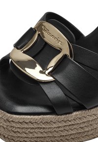 Sandali neri con piattaforma caratterizzati da un ampio design a incrocio e una grande fibbia dorata. La suola presenta una texture in iuta intrecciata per un tocco in più.