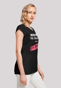 Black t-shirt with short sleeves, featuring white and pink text graphics. Rounded neckline, relaxed fit, and soft fabric texture.