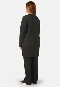 Top lungo a maniche lunghe nero con scollatura tonda abbinato a pantaloni coordinati. Il tessuto è strutturato, presenta una vestibilità rilassata e fessure laterali.