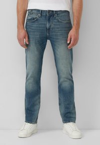 Wyblakłe niebieskie dżinsy o prostym kroju, pięć kieszeni i subtelne przetarcia, w zestawieniu z białymi sneakersami i prostą białą koszulką.