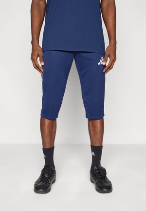 Marineblaue Sportsshorts mit drei weißen Streifen und Logo an der Seite, kombiniert mit schwarzen Schuhen und passenden dunklen Socken. Glatte Stoffstruktur.