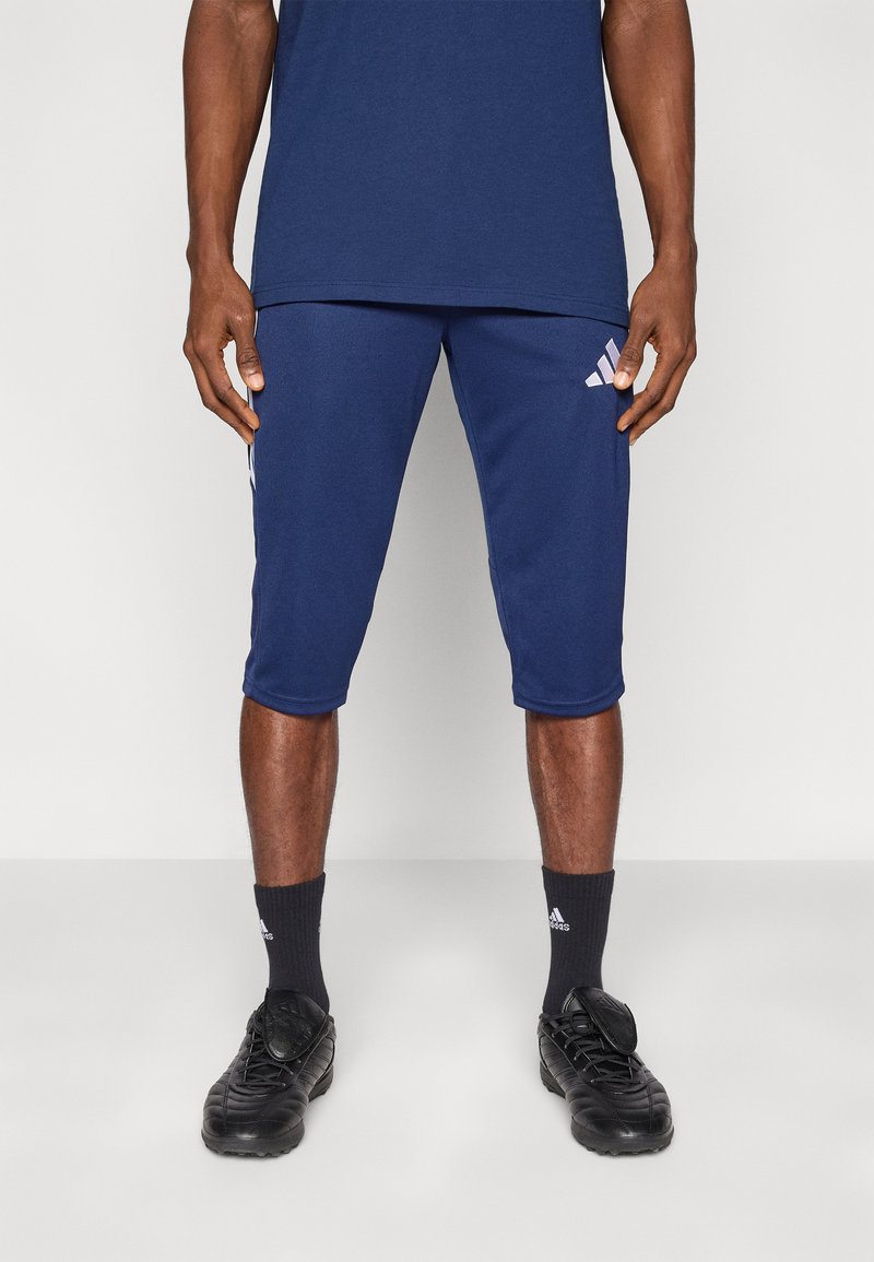 Ναυτικά αθλητικά σορτς με τρεις λευκές ρίγες και λογότυπο στο πλάι, συνδυασμένα με μαύρα παπούτσια και αντίστοιχες σκοτεινές κάλτσες. Υφασμάτινη υφή λείας επιφάνειας.