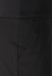 Svart tyg med en mjuk textur har en sidficka och sömdetaljer. Designen är minimalistisk och skräddarsydd i formen.